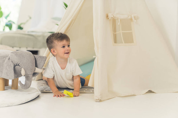 menino bonito caucasiano brincando em sua tenda na sala de estar, conceito de crianças. Foto de alta qualidade - Foto, Imagem