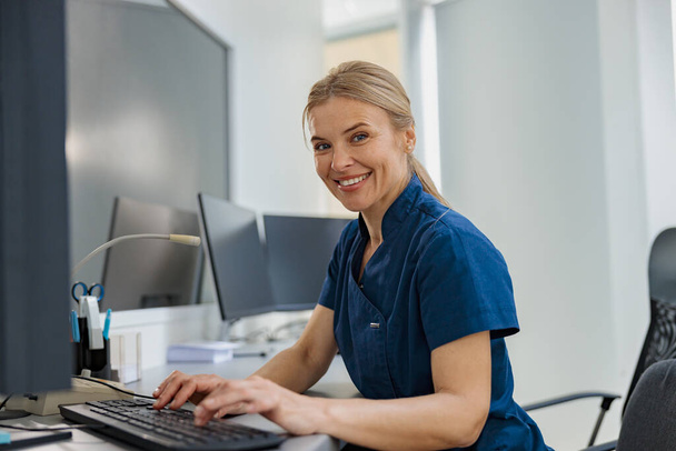 Медсестра з Дюті працює над комп'ютером у приймальному стенді в сучасній клініці. Фотографія високої якості - Фото, зображення