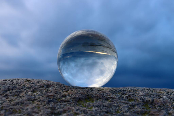 Crystal ball on the beach, sitting on a boulder, dark clouds reflecting in the ball, pending storm - Zdjęcie, obraz