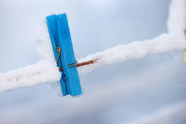 Один замерзший синий деревянный колышек, покрытый снегом на линии. Старая деревянная прищепка на бельевой веревке в ледяном саду. Старомодный инструмент для свежеочищенного белья в росовый холодный зимний день. - Фото, изображение