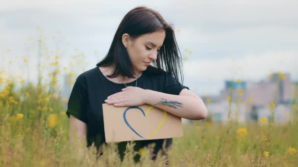 Ελκυστική καυκάσιος νεαρός έφηβος γυναίκα πατριώτης σταθεί έξω κρατήστε πολύχρωμο χαρτόνι σχέδιο αγάπη σχήμα καρδιά σημάδι σε χρώματα Ουκρανοί μπλε κίτρινο δείχνουν εθνικό σύμβολο των ρομαντικών συναισθημάτων - Πλάνα, βίντεο