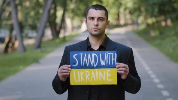 Portrait sad serious man activist patriot guy stand outdoors hold cardboard with written inscription stand with Ukraine protests against military conflict demonstrate opposition anti violence banner - Felvétel, videó