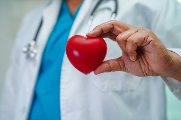 Ασιάτισσα γιατρός κρατώντας κόκκινη καρδιά για την υγεία στο νοσοκομείο. - Φωτογραφία, εικόνα