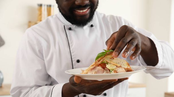 Male African-American chef with tasty caesar salad in kitchen - Foto, afbeelding