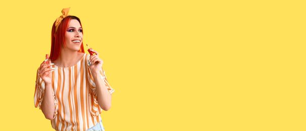 Stylish transgender woman applying lipstick against yellow background with space for text - Фото, изображение