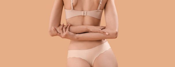 Slim young woman in underwear on beige background, back view - Photo, image