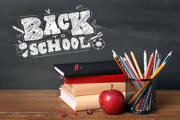 Stationery and  apple on table near blackboard with text BACK TO SCHOOL - Photo, image
