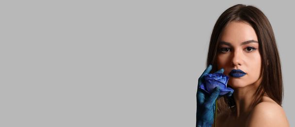Stylish young woman with painted hand, blue lipstick and rose on grey background with space for text - Foto, Imagen