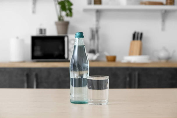 Бутылка и стакан чистой воды на кухонном столе - Фото, изображение