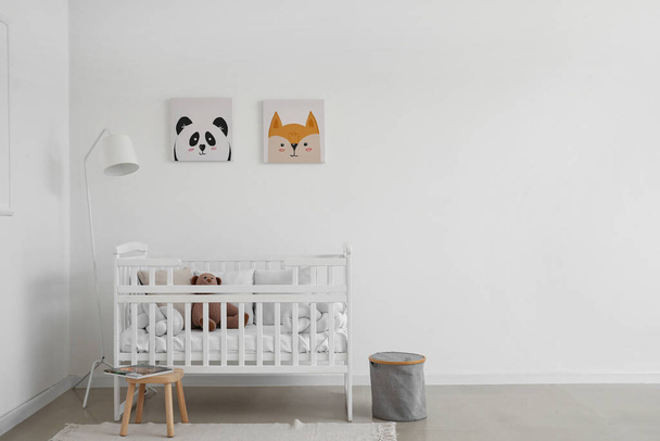 Interieur van lichte kinderkamer met babybedje, lamp en kruk - Foto, afbeelding