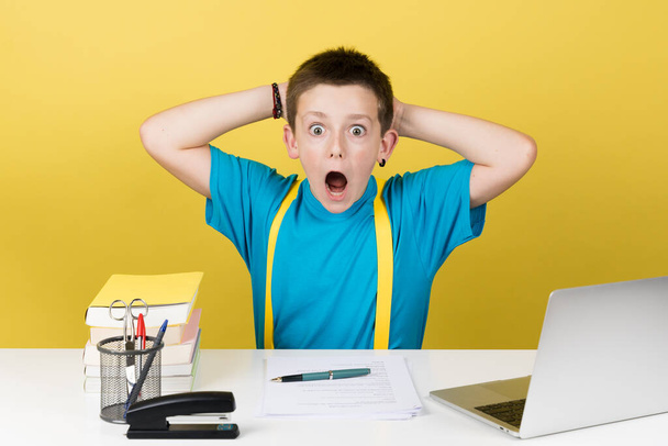 Surprised cute student boy looking at camera hands behind head isolated on yellow background. - Photo, Image