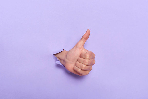Close up of person's hand with thumb up through hole in purple paper wall, demonstrating approval like gesture, satisfaction of done work. Banner for sales. - Zdjęcie, obraz