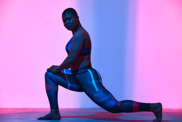 Body positive. African american woman in sportswear workout, fashion studio shot. Advertising photo, copyspace. Gradient pink and blue background - Foto, imagen