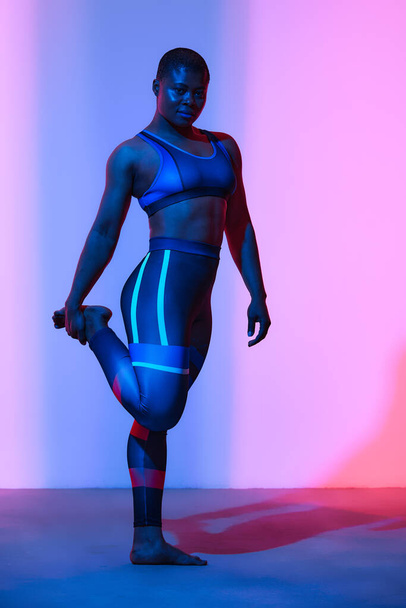 Body positive. African american woman in sportswear workout, fashion studio shot. Advertising photo, copyspace. Gradient pink and blue background - Fotografie, Obrázek