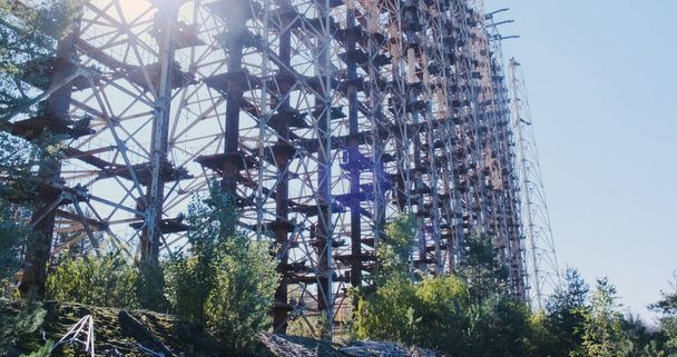 Металлическая стена радиолокационных антенн. Солнце светит сквозь строение. Промышленный, заброшенный военный радар в лесу, Чернобыль, Украина. Высококачественные 4k кадры - Фото, изображение