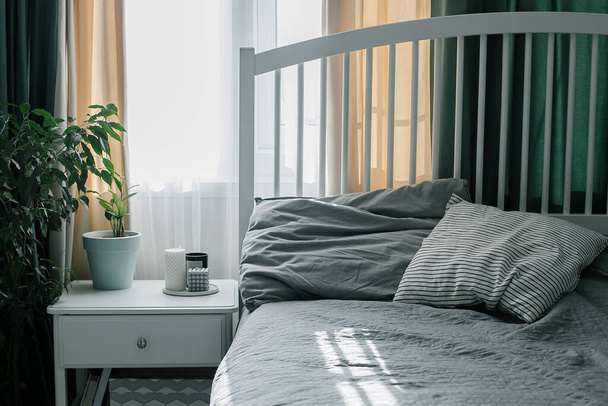 Bedroom with light interior. Modern candle, home plant on bedside table near bed. Home lifestyle. - Fotografie, Obrázek