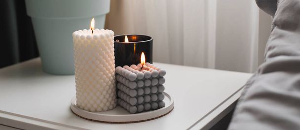 Modern burning candle on bedside table near bed. Home aroma. Wellness. Banner image for design, web site - Fotó, kép