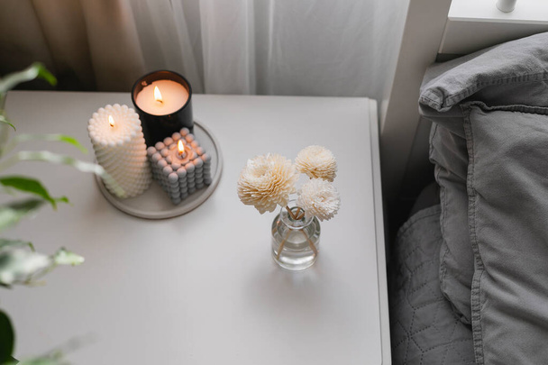 Aromatic reed air freshener and burning candle on bedside table in the bedroom. Home aroma. Wellness, wellbeing - Foto, Bild