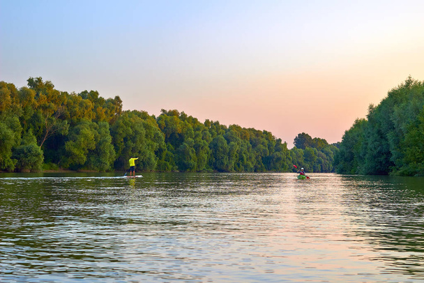 Hombre en stand-up paddle board SUP y mujer en kayak verde remando por la mañana en el río Danubio - Foto, Imagen