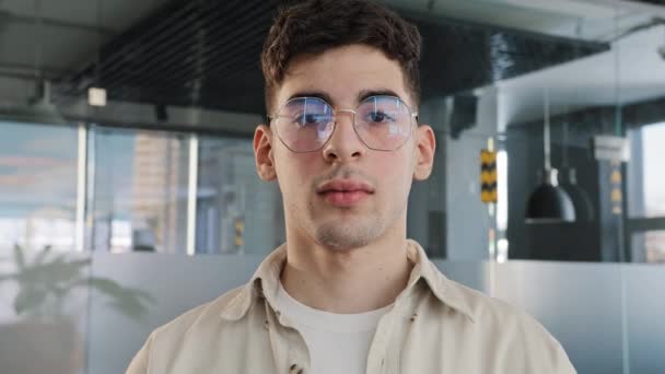 Close-up caucasian serious puzzled clever guy student in glasses looking at camera posing indoors young man with sad expression feeling upset male manager focused standing in office space portrait - Séquence, vidéo