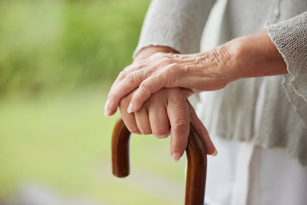 Zbliżenie starszych niepełnosprawnych kobiet ręce trzymając laskę na zewnątrz w ogrodzie lub parku. Starsza kobieta uczy się chodzić po udarze. Palce starszej pani z pomoca chodu, potrzebujacej pomocy z równowaga. - Zdjęcie, obraz