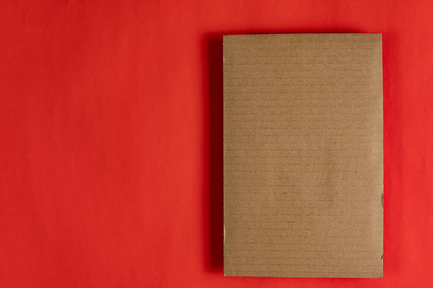 Ένα ορθογώνιο κομμάτι καφέ χαρτονιού πάνω σε κόκκινο φόντο. Αντιγραφή χώρου για στοιχεία κειμένου και σχεδιασμού. Άνω όψη. - Φωτογραφία, εικόνα