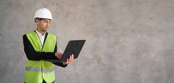 Muslim civil engineer using laptop. Engineering and construction concept. Engineer with laptop computer. Man in hard hat. Architect in yellow vest on grey background. Banner, space for text - Foto, imagen