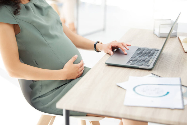 Closeup shot of a pregnant businesswoman working on a laptop in an office. - Фото, зображення