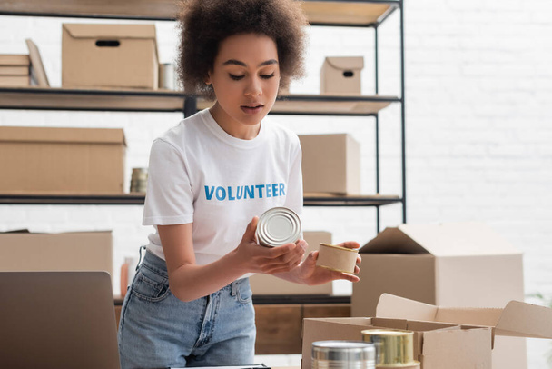 young african american woman sorting canned foodstuff in volunteer center - Photo, Image