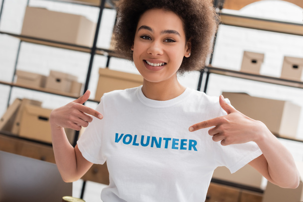 happy african american woman pointing at volunteer lettering on t-shirt in charity center - Fotografie, Obrázek