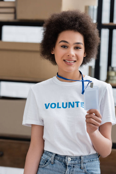 χαμογελαστή Αφροαμερικανή γυναίκα που κρατά λευκή ετικέτα ονόματος στο κέντρο εθελοντών - Φωτογραφία, εικόνα