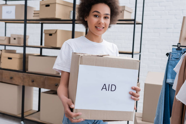 улыбающийся африканский волонтер держит коробку с надписью "Помощь" в благотворительном центре - Фото, изображение