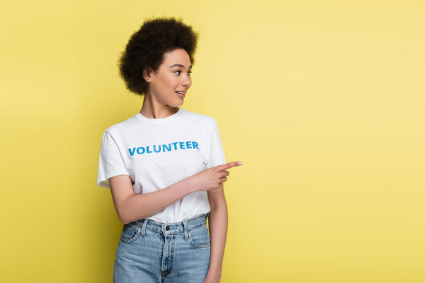 african american woman in t-shirt with volunteer lettering pointing with finger isolated on yellow - Foto, Imagem
