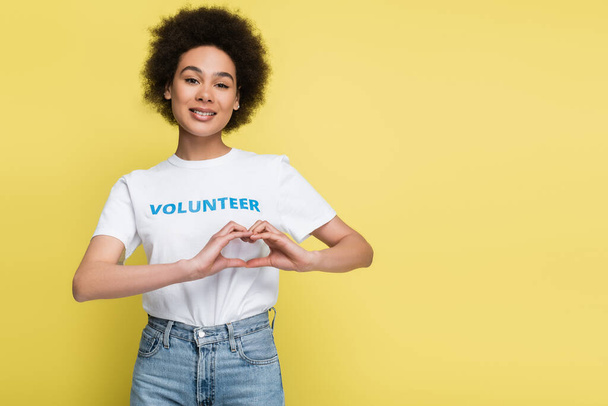 mujer afroamericana en camiseta con letras voluntarias que muestran un signo cardíaco aislado en amarillo - Foto, Imagen