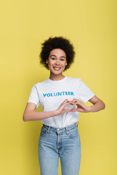 young african american volunteer showing heart symbol with hands isolated on yellow - Foto, imagen