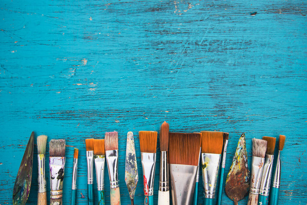 Artistic art supply utensils with paintbrushes on turquoise wooden background with copy space. Flat lay photo - Foto, Bild