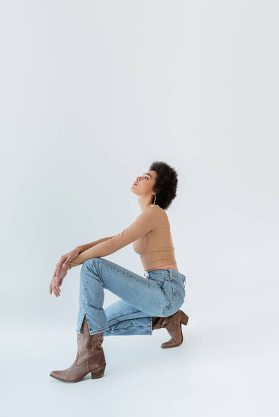 side view of african american model in jeans and cowboy boots on grey background - Fotó, kép