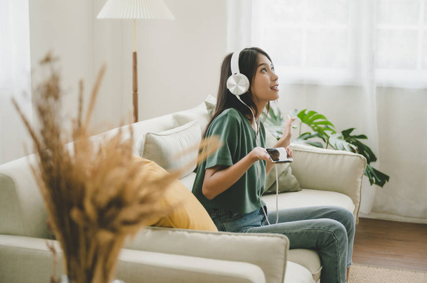 Азійські жінки слухають музику у вітальні. Вона сиділа на дивані й відпочивала на вихідних. - Фото, зображення