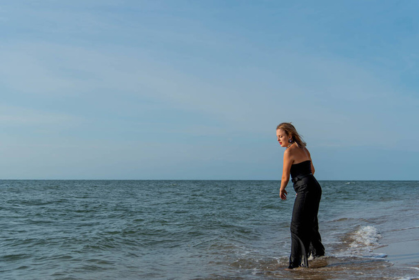 Female wearing black dress walking on beach. See view - Zdjęcie, obraz