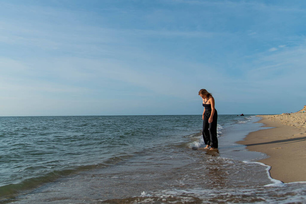 Beautiful girl wearing black dress walking on beach. See view - Zdjęcie, obraz