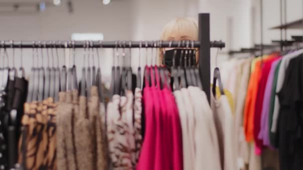 Kypsä valkoihoinen nainen shopper valitsee vaatteita vaatekauppa tyylikäs keski-ikäinen nainen asiakas pukeutuu suojaava naamio etsivät sopivaa täydellinen asu ripustimet myynti alennus ostaa ostoksia - Materiaali, video