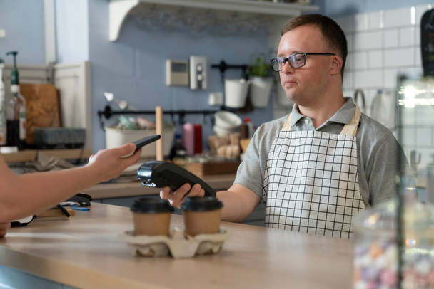 Caucasian man with down syndrome accepting contactless payment in the cafe - Fotoğraf, Görsel