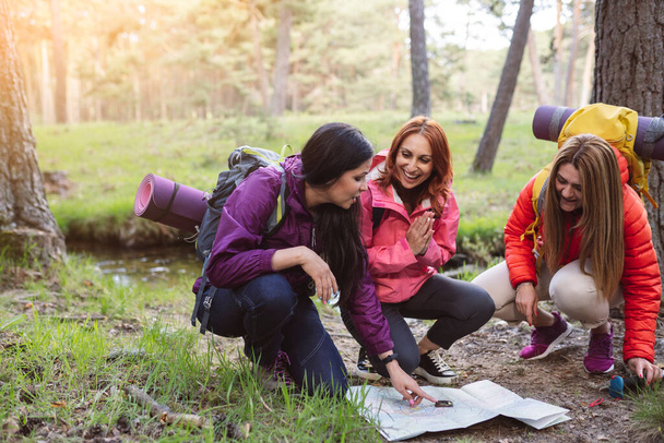 group of mature female friends looking at map in nature, real women traveling backpackers. - Foto, imagen