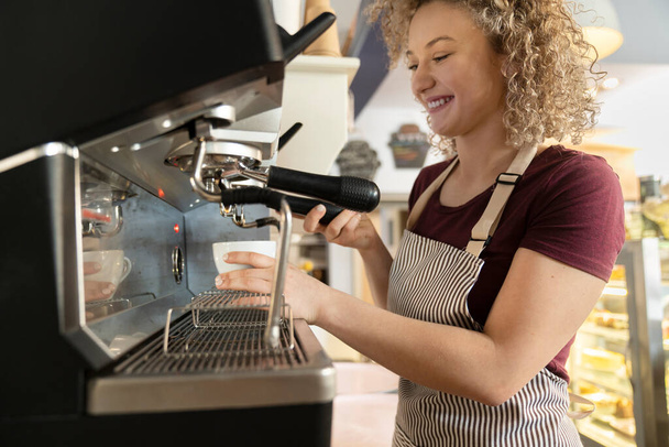 Νεαρή καυκάσια μπαρίστα που φτιάχνει καφέ στο καφέ με μεγάλο χαμόγελο - Φωτογραφία, εικόνα