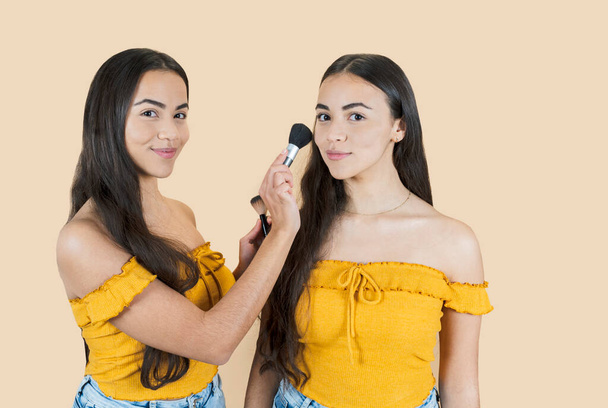 Beautiful and young twin sisters having fun and laughing in the studio on a beige background make-up. - Foto, Imagem