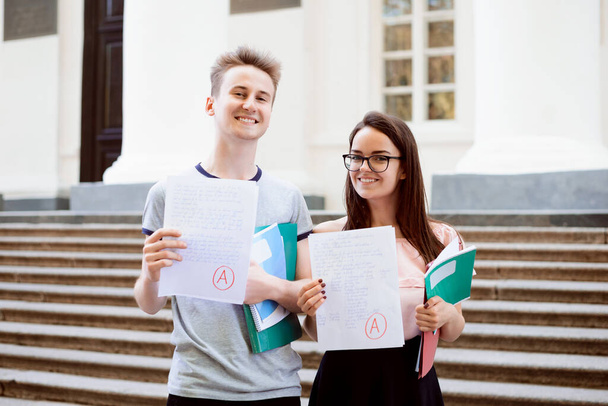 Male and female teenagers standing in front of university showing excellent results of entrance exam, happy to become students of a popular university and study hard - Valokuva, kuva