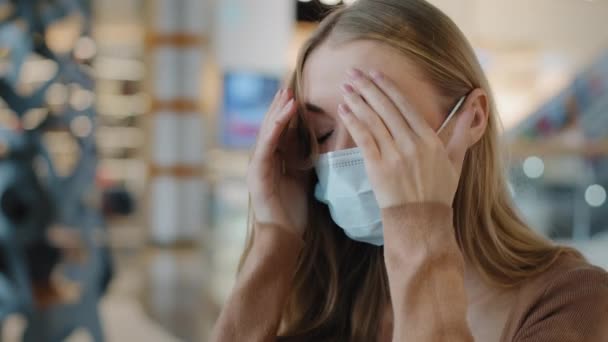 Běloška dáma nemocná trpí blondýny dívka nemocná žena nosí lékařskou masku držení spánků čelo pocit strachu chřipka virus příznaky koronavirus pandemie pocit nevolnosti špatné bolesti hlavy - Záběry, video
