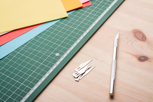 Скальпель для паперу і набір лопатей на столі біля ріжучого килимка з різними кольоровими паперами
 - Фото, зображення