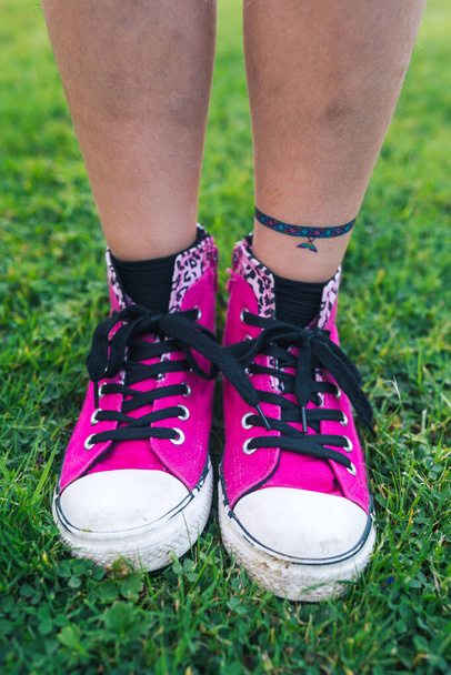 Una chica con elegantes zapatillas de deporte de color rosa de pie sobre hierba verde fresca - Foto, imagen