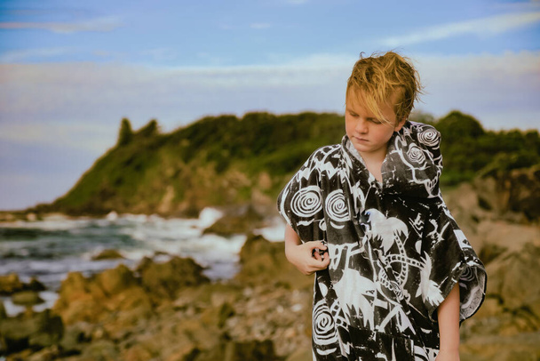 Junge mit Kapuzenhandtuch nach dem Schwimmen auf Felsen in der Touristenattraktion The Tanks in Forster, NSW Australien - Foto, Bild